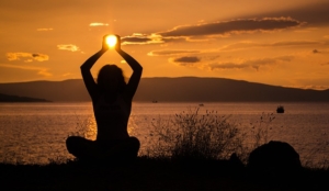 Silhouette of a person seemingly holding the Sun in their hands during a sunset, representing benefits of living in a waterfront property